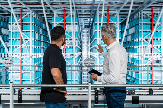 Businessman pointing at storage rack and explaining coworker in industry