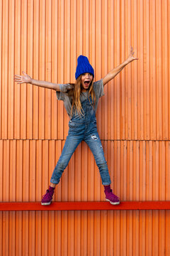 Young girl wearing dungarees, orange wall in the background