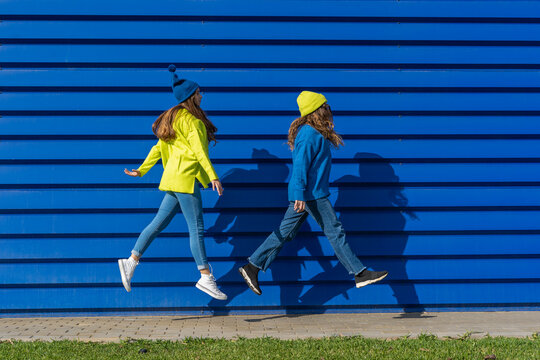 Two teenage girls wearing matching clothes jumping in the air in front of blue background