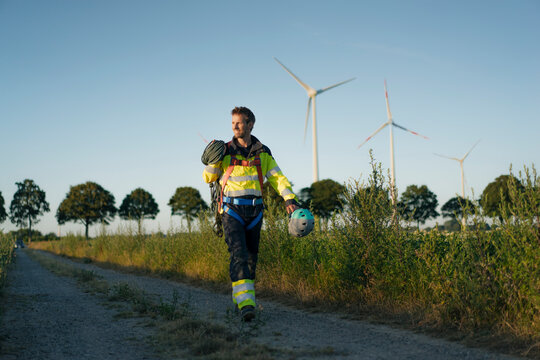 Technician walking on field path at a wind farm with climbing equipment