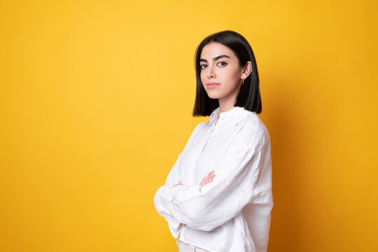 Young woman standing with arms crossed against yellow background