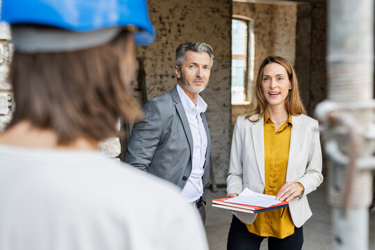 Female colleague talking with construction worker while standing by male architect