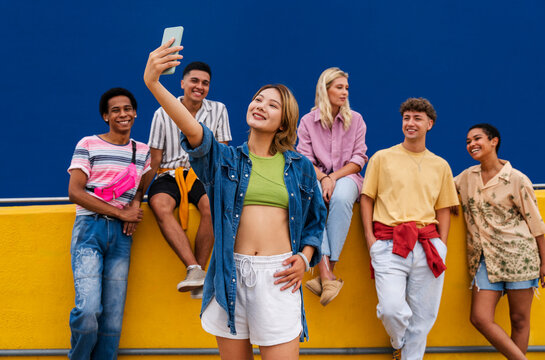 Confident young woman standing in front of group of friends taking a selfie