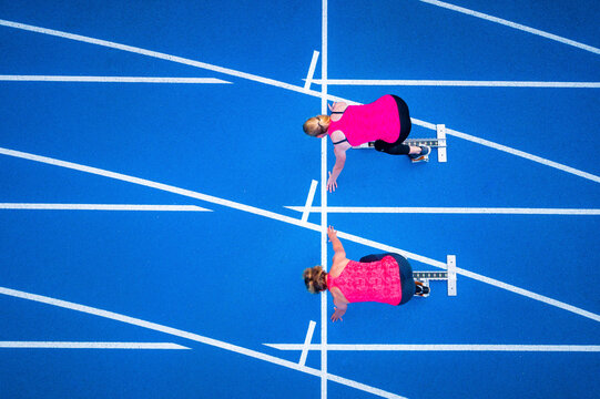 Top view of two female runners starting on tartan track