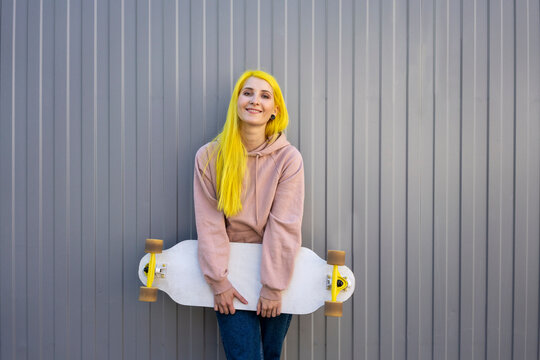 Young woman holding skateboard standing against metal wall