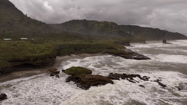 Drone flying forward over the rocky seashore with strong waves from the ocean at Truman Track, West Coast of South Island