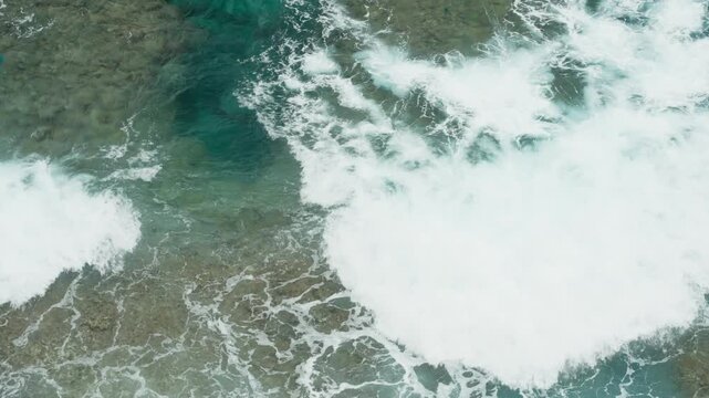 Top view of ocean waves breaking over rocky coastline with turquoise water and white foam