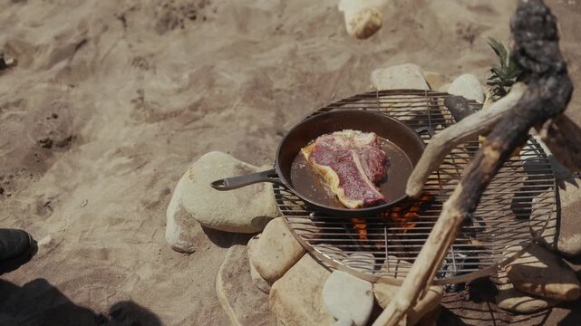 Cooking a T-bone steak in a cast iron pan over an open fire