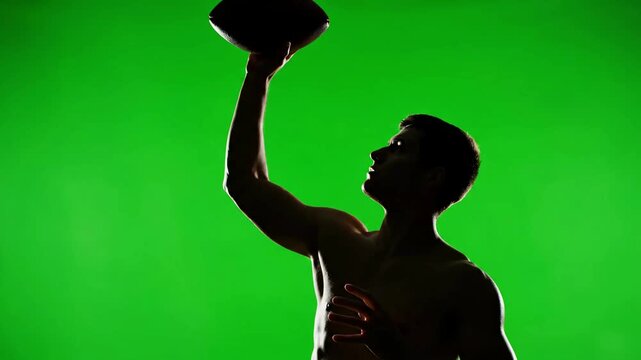 Silhouette of American Football Player Holding Ball Up in Victory Against Green Screen Background