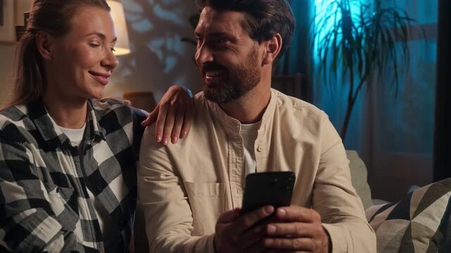 Happy Caucasian middle-aged couple using mobile phone app together looking in smartphone satisfied shopping online buying ordering food delivery family husband with wife woman man at evening home