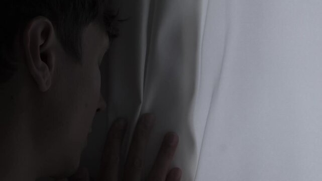 Social anxiety and isolation concept with introvert person cautiously looking through curtain, loneliness, emotional stress and mental discomfort atmosphere. Close-up portrait