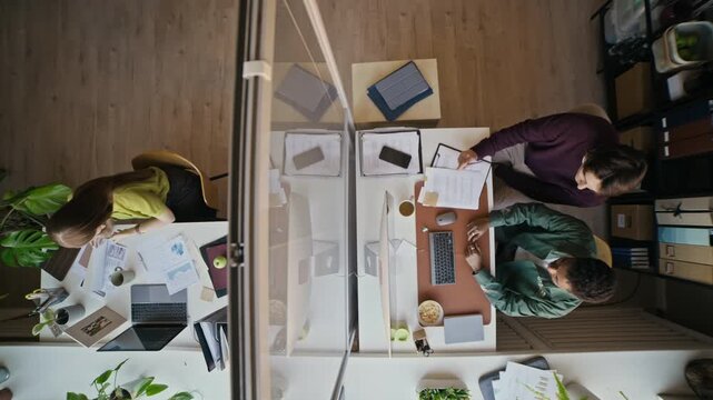 Overhead office scene with professionals having discussion while organizing documents and working on computers in modern environment