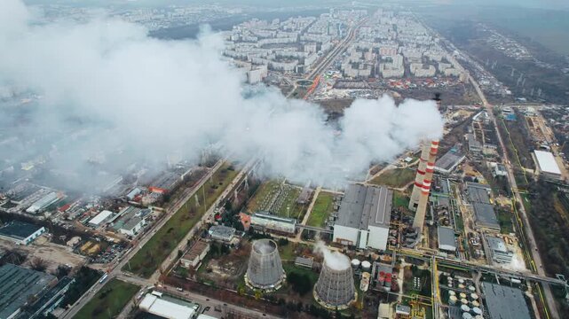 Industrial power plant with smoke stacks emitting thick white vapor clouds over urban city district.