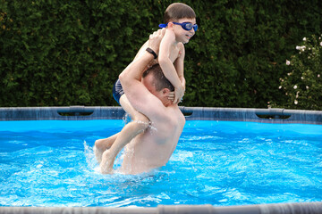 Naklejka premium Father and son spend time together playing in backyard pool. Caucasian man and boy in swimming goggles having summer fun, outdoor leisure, active lifestyle. Summertime family pleasure. Enjoy moment.