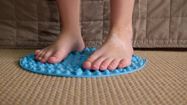 Child performing foot massage on orthopedic mat. Close-up of a child's bare feet walking on a blue orthopedic acupressure mat for flatfoot prevention and sensory stimulation, improving balance