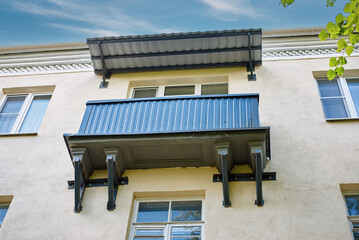 Reinforced apartment balcony. Old residential building facade, newly renovated balcony with corrugated metal siding and protective canopy roof supported by heavy steel wall brackets. Structural repair © Tricky Shark