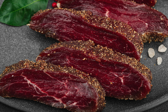 Sliced seasoned raw beef filet tenderloin on a dark plate, garnished with bay leaves, sea salt