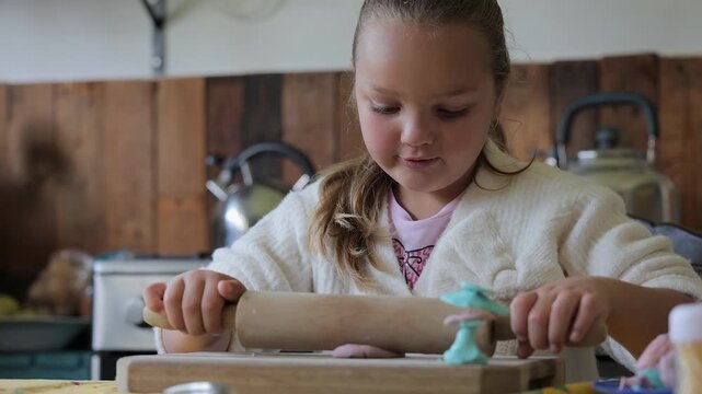 Young girl flattens clay with rolling pin at craft table, close up