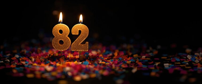 Festive number 82 candle shining brightly with colorful confetti against black backdrop