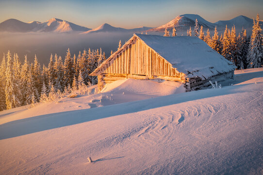 Abandoned wooden cabin in snowy winter mountains at sunrise