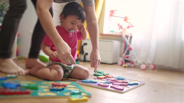 baby daughter plays with toys on the floor develops fine motor skills. Mom plays with her baby lifestyle daughter, teaches her to put pictures into slots. happy family kid dream concept