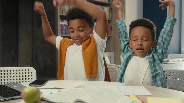 Two African American little boys siblings kids tired studying yawning stretching writing homework learning overworked brothers children school pupils sons write e-learning study learn yawn stretch