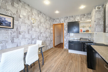 Fototapeta premium cozy kitchen-dining area with cityscape wallpaper, black cabinetry, granite countertops, and a dining set with white quilted chairs under recessed lighting