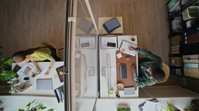 Overhead shot of office coworkers working at separate desks with laptops, documents and smartphones in modern workspace
