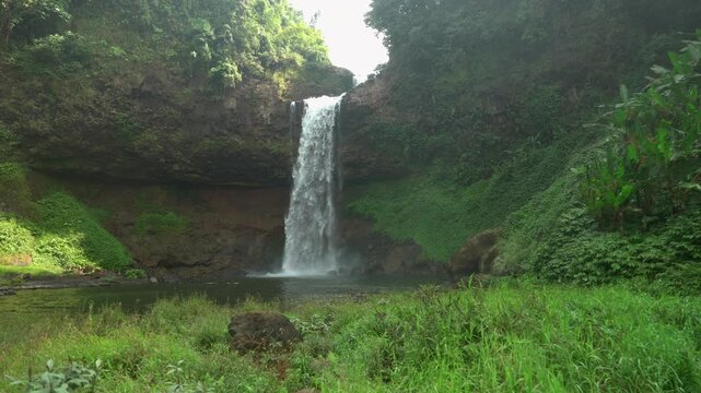 Slow motion optical zoom shot of Tad E-Tu waterfall plunging into a misty pool surrounded by lush forest on the Bolaven Plateau.