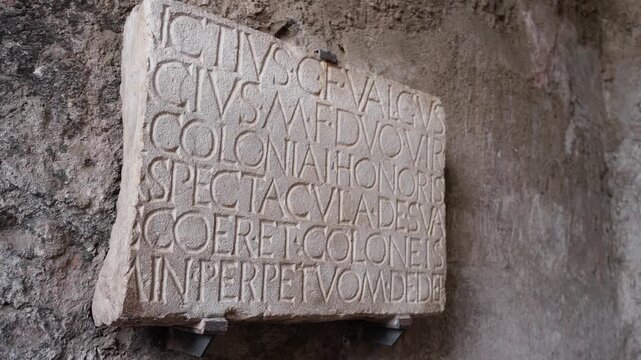 Ancient Latin inscription tablet in Pompeii, carved into pale stone and mounted on a weathered wall, showing Roman civic text in close detail.