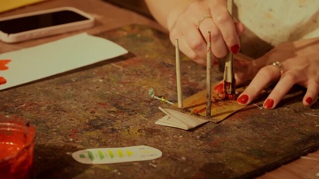 A woman's hands with red nails apply red ink through a stencil on a worn studio table in a Kyoto craft workshop.