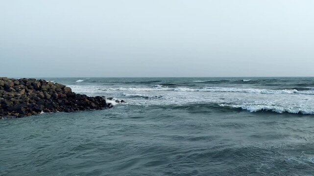 Wide moody seascape of rolling Arabian Sea waves beside stone breakwater at Dwarka. Ideal for pilgrimage travel, overcast coastal India, spiritual documentary and nature projects.