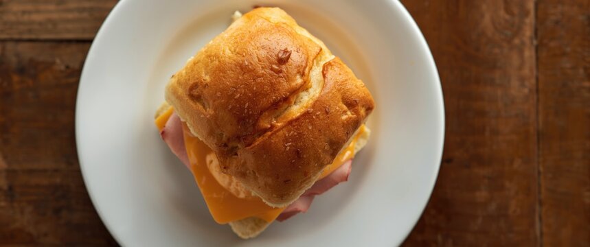 Close overhead image of Hawaiian roll slider with ham and cheese on white dish over wood