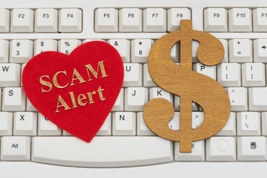 SCAM Alert text on a red heart with a dollar sign on a white computer keyboard for dating scams