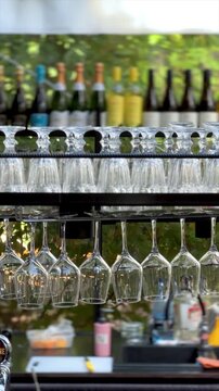 Rows of hanging wine glasses at outdoor bar, elegant glassware and bottles in hospitality setting