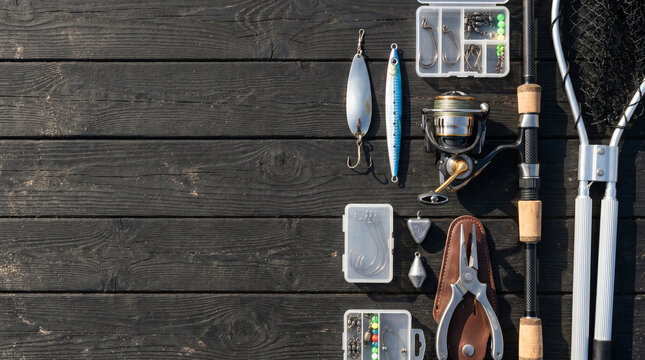 Flat lay composition of fishing accessories including reel, hooks and artificial lure on wooden table with copy space.