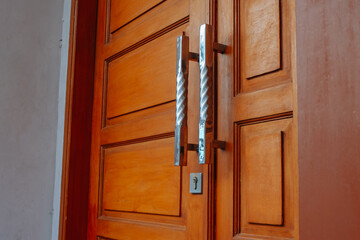 A detailed shot focusing on the polished chrome handles of a solid, warm-toned wooden door © awgraphoto