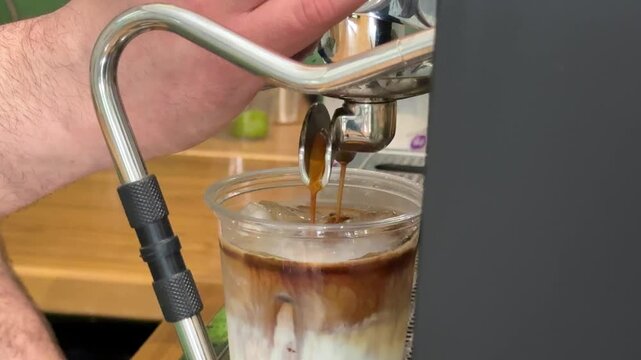 Preparing iced latte in plastic cup with milk coffee and ice cubes