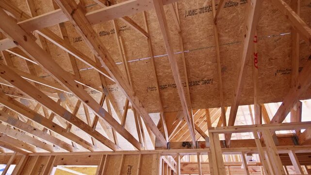 Workers are installing wooden beams to build roof frame at construction site