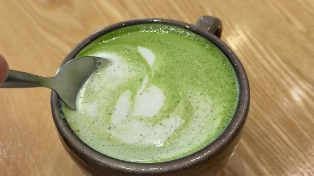 Scooping fluffy foam from matcha latte with teaspoon in gray ceramic cup