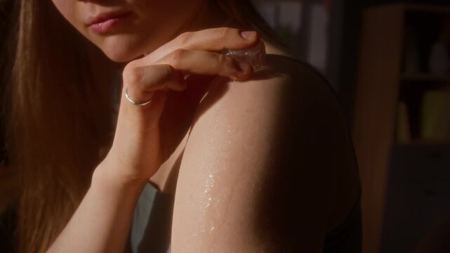 Close up shot of young woman running ice cube across skin on bare arms and enjoying cold sensation in summer heat, scene lit with sunlight, copy space