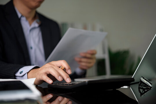 Executive checking financial report using calculator laptop office. Business administration data analysis tax return modern workspace checking revenue loss.