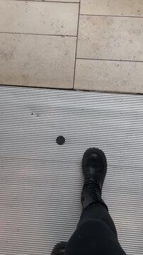 Boots on stone tile floor closeup showing grout lines and subtle scuff marks, slow step, neutral beige texture. POV boots on ceramic tiles in shopping mall or public indoors