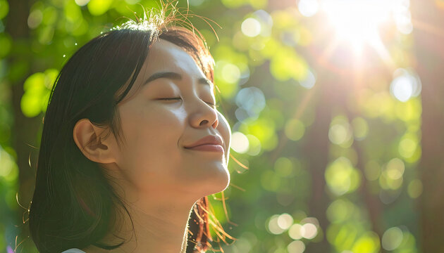 Young woman breathing fresh forest air with eyes closed, warm sunlight filtering through trees, peaceful nature therapy concept, environmental health and wellness goals. Close-up.