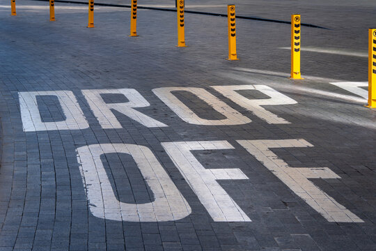 Large drop off zone pavement marking on a paved urban area with yellow safety bollards, suitable for transportation, parking, passenger pickup and traffic management concepts.