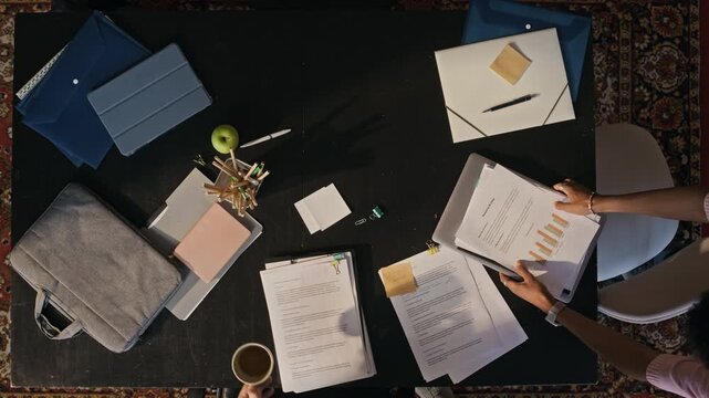 Overhead office scene with professionals examining charts, reports and documents during productive meeting