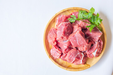 Fototapeta premium Fresh raw beef meat slices in a wooden plate on white background with copy space. Lamb red meat chopped in small cuts ready for skewers. Top view with space for your text