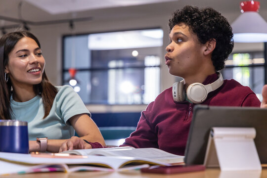 Diverse students studying and discussing notes at campus lounge with textbooks, tablet, headphones