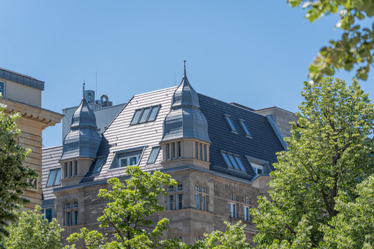 Historic Berlin roofline with turrets, windows, and leafy deciduous trees under clear blue sky. Elegant city architecture scene for travel, heritage, real estate, and tourism.