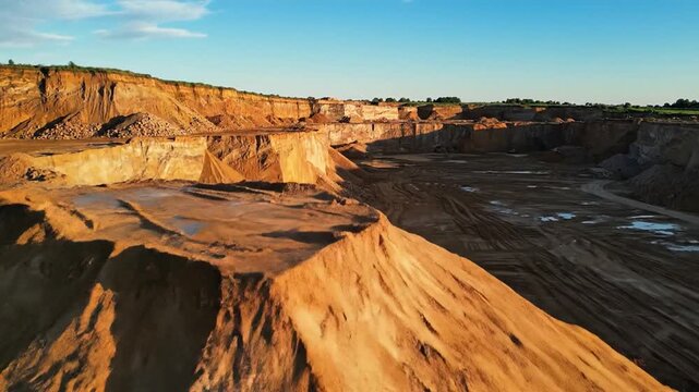 Dramatic golden earth mounds and towering quarry walls under a bright blue sky, showcasing immense excavation and natural formations.